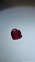 Heart-shaped vivid red hot pink natural ruby gemstone, showing clear facets and polished surface.