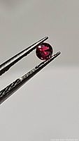 Close-up photo of a vivid electric red round ruby held with tweezers showing color and clarity.