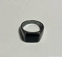 Front view of the men's ring showing the square black onyx stone set on a black metal band.