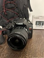 Front view of Canon EOS Rebel T6 with attached 18-55mm lens and backpack in background