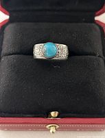 Front view of Navajo silver ring with turquoise center stone and engraved band inside a jewelry box