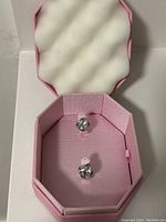 Pair of Swarovski stud earrings with clear, faceted crystal stones set in silver-tone metal inside a pink octagonal jewelry box with satin interior.