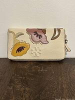 Front view of Tory Burch clutch purse showing cream leather with multicolor floral appliqué and embossed logo