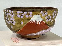 Front side of ceramic bowl showing hand-painted Mt. Fuji and cherry blossoms design with gold outline on a brown background.