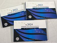 Three unopened American Innovation $1 Coin Proof Sets for years 2022, 2023, and 2024 in original retail packaging, featuring blue, white, and black design with stars.