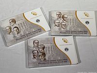 Three original presentation folders for 2013, 2014, 2016 U.S. Mint Presidential $1 Coin Proof Sets showing artistic portraits of presidents on the covers.