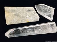 Three polished quartz crystal specimens on black background, showing different angles and sizes