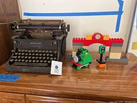 Full view of Woodstock antique typewriter and adjacent Thomas the Train Duplo set including train figure and accessories on a wooden surface