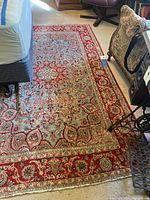 Full view of the red, blue, beige patterned area rug placed partially under furniture in a room with carpeted floor.