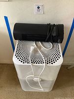 White Blueair air purifier with black Lasko tower fan/heater on top, cords visible.