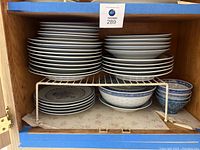 Two stacked sets of blue and white dishware inside a wooden cabinet showing plates, serving bowl, soup bowl, and dipping bowls.