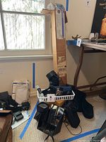 Overall view showing assorted lenses, accessories, wood blocks, and cables in a pile on the floor near window and table.