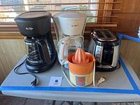 All four appliances on table: two Mr. Coffee coffee makers (black and white), Hamilton Beach toaster, and Dominion juicer