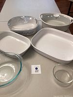 View of two large oval covered casserole dishes with lids and two large rectangular casserole dishes and two clear Pyrex mixing bowls, all white or clear glass with signs of use.