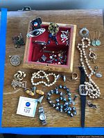 Full layout of costume jewelry including necklaces, brooches, earrings, a ring and a wristwatch on a wooden surface