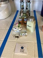 Various salt and pepper shakers including tall glass, cream ceramic, and smaller wilderness scene painted pairs; small floral covered dish; tiny cat teapot; silver-tone ornate frame accessory; rectangular floral planter