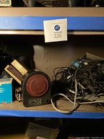 Shelving with old camera equipment, including a machine with a red circular part and bundles of cables
