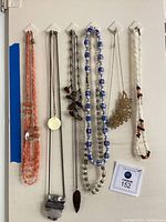 Photo of seven hanging necklaces showing orange beads, jade pendant, crystal and pearl strands, and silver floral pendant