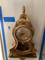 Full front view of gold-tone Zenith clock showing shape, painted floral details and 19×11″ measurement tag