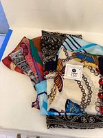 Scarves fanned out showing different colors and patterns including light background with chains and butterflies, black and white florals, and blue stripes.