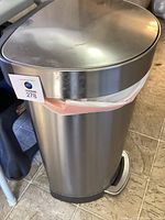 Full side view of stainless steel step trash can with plastic trash bag fitted under lid and pedal visible at base.