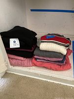 Two stacks of folded women's sweaters, showing colors and fabric textures, placed on a white shelf.