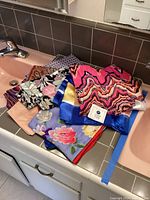 Overview of all scarves displayed on a bathroom counter, showing variety in colors and general size.