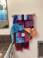 Full view of multiple scarves hanging on a rack showing various colors and patterns including polka dots, floral embroidery and fringe details.