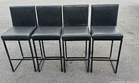 Front view of 4 black upholstered barstools with metal legs showing seating and backrest alignment.