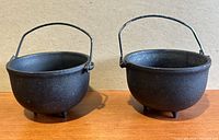 Two black cast iron pots seen from a three-quarter angle showing handles and legs.