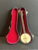 Miniature banjo toy in its form-fitted red velvet-lined case, showing the toy inside the case.