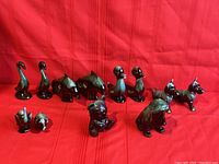 12 vintage Blue Mountain Pottery animal figurines arranged on a red cloth background.
