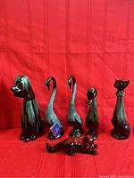 Front view of all six Blue Mountain Pottery animal figurines on red cloth background including dog, swans, duck, cat, and raccoon.