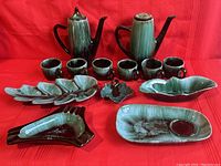Full front view of entire 13 piece Blue Mountain Pottery set on red background showing cups, teapots, and serving dishes.