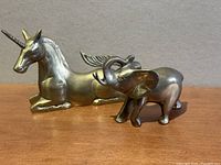 Front view of the two brass animal statues on wooden surface against plain background, showing unicorn lying down and elephant standing.