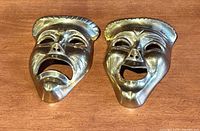 Photo of both brass masks side-by-side on a wooden surface, showing detailed facial expressions.
