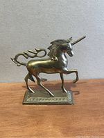 Photo showing the left side profile of the brass unicorn figurine on its base against plain background