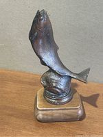 Front angle view of the bronze/brass salmon sculpture mounted on wooden base, showing the fish jumping upward with detailed scales and fins.