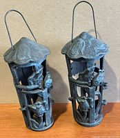 Pair of vintage cast iron garden candle holders with decorative bird and flower designs and curved metal handles. Front view.