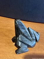 Side angle showing the carved angular limbs and glossy stone surface of the frog figurine with visible gold sheen.