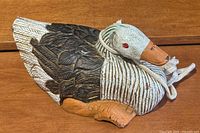 Front diagonal view of vintage folk art wooden duck showing detailed painted feathers, carved texture, orange beak and feet, and white rope tied around the neck.