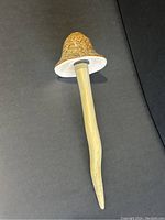 Photo showing the mushroom shaped top of the garden stick against a dark background, highlighting the texture and color of the cap and the smooth stem.