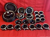 Set displayed on red surface with plates, saucers, cups, and covered serving dish in a brown glaze with speckled rim.