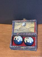 Pair of blue Baoding chime balls decorated with white enamel elephants inside open blue fabric-covered box with red interior, showing health ball direction paper insert