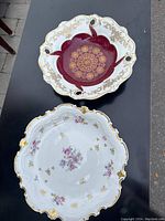 Both porcelain plates displayed on black background showing their ornate floral and gold decorative patterns.
