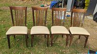 Front view of four walnut wood dining chairs with cream leather seats placed on grass outdoors.