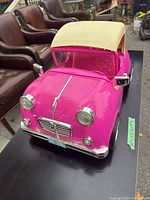 Front angle view of the hot pink retro convertible toy car with cream fabric convertible top showing chrome headlights and grille details.