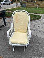 Front view of white wooden armchair glider with yellow cushions and some paint chips