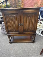 Front view of a dark wood cabinet with two doors featuring decorative carved panels and round metal handles.