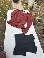 Two clothing items laid on outdoor surface: rust-purple woven blazer with black leather shoulders and charcoal gray sleeveless V-neck top.